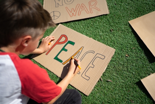 Kleine jongen kleurt de letters PEACE in op een protestbord